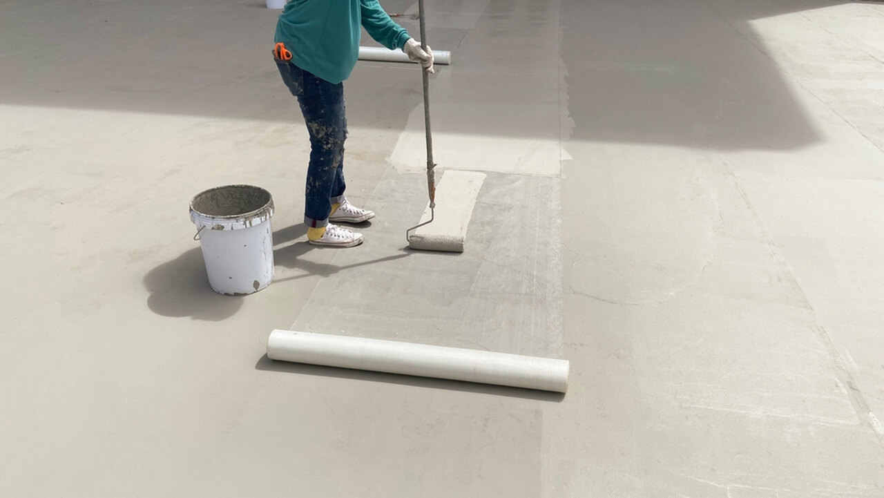 worker applying waterproofing admixture to the floor with a long brush