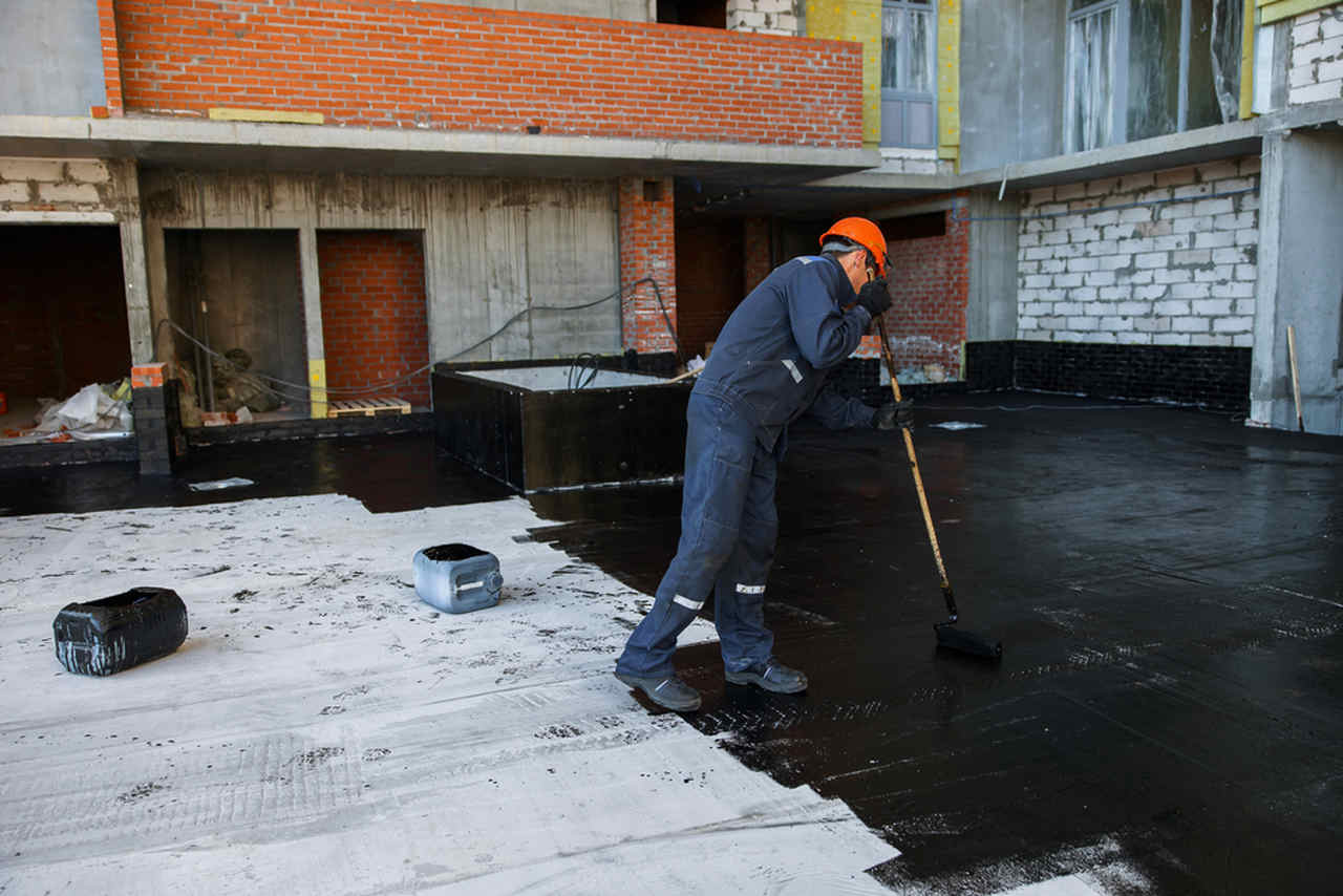 worker applying water insulation to the floor with long brush
