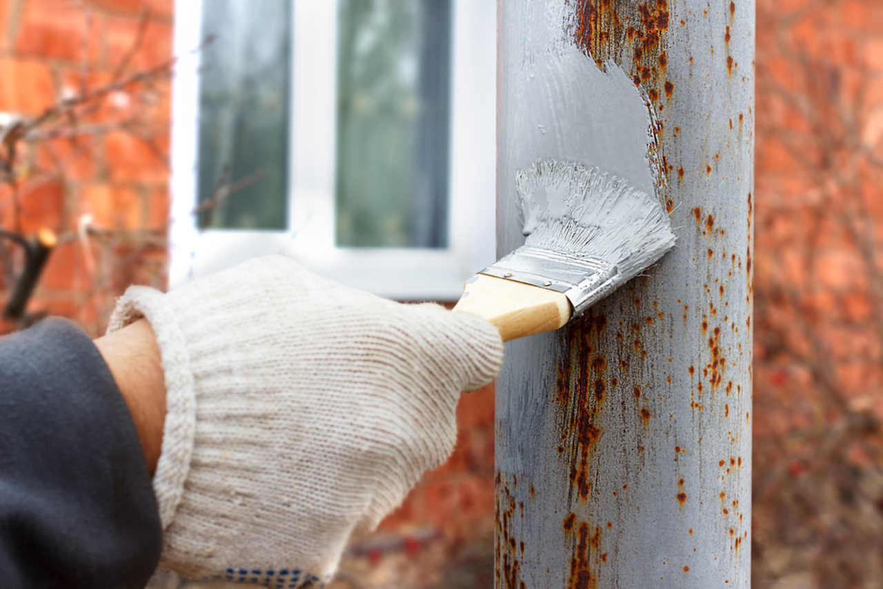 worker appyling primer paint to the rusty post