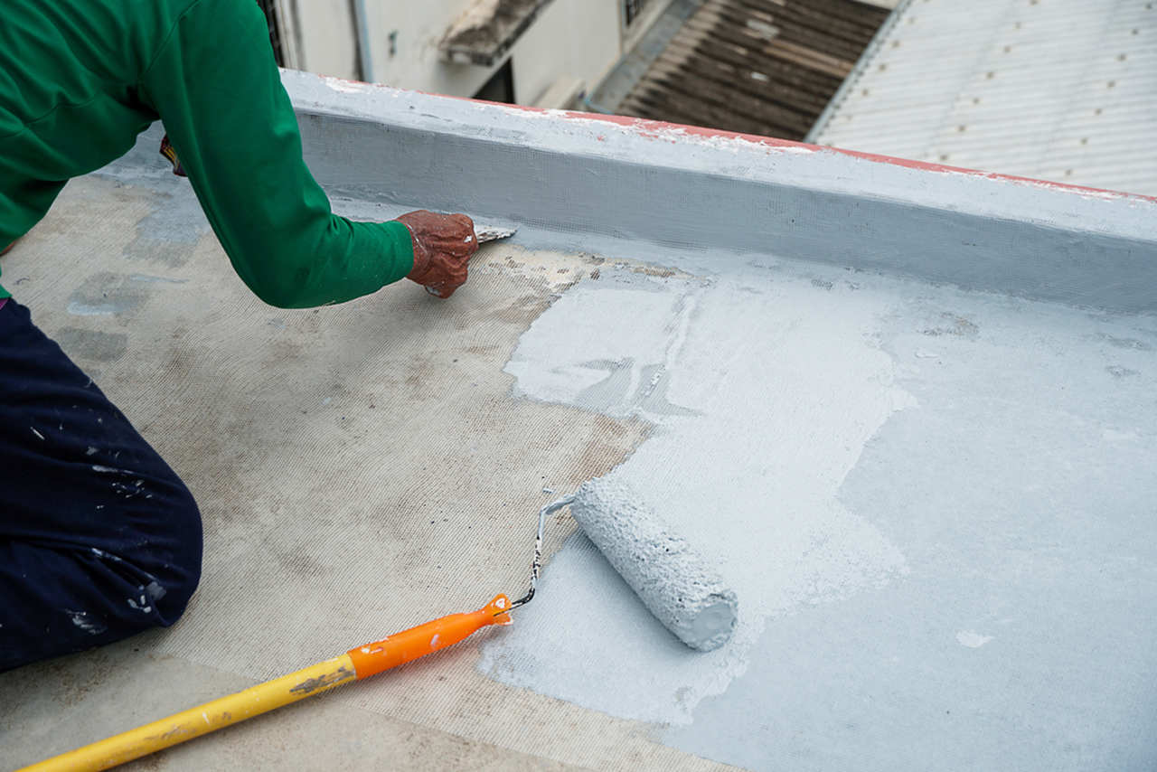 eğilerek çatı kenarlarına su yalıtım malzemesi uygulayan işçi